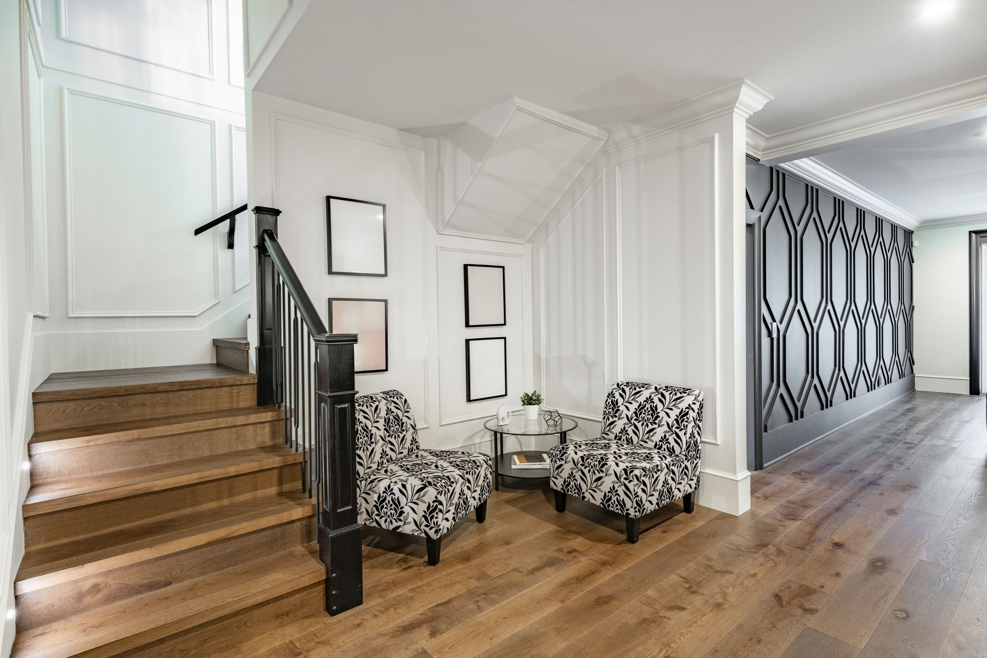 Bright entryway with wooden stairs, two patterned chairs, and a long hallway with geometric wall décor