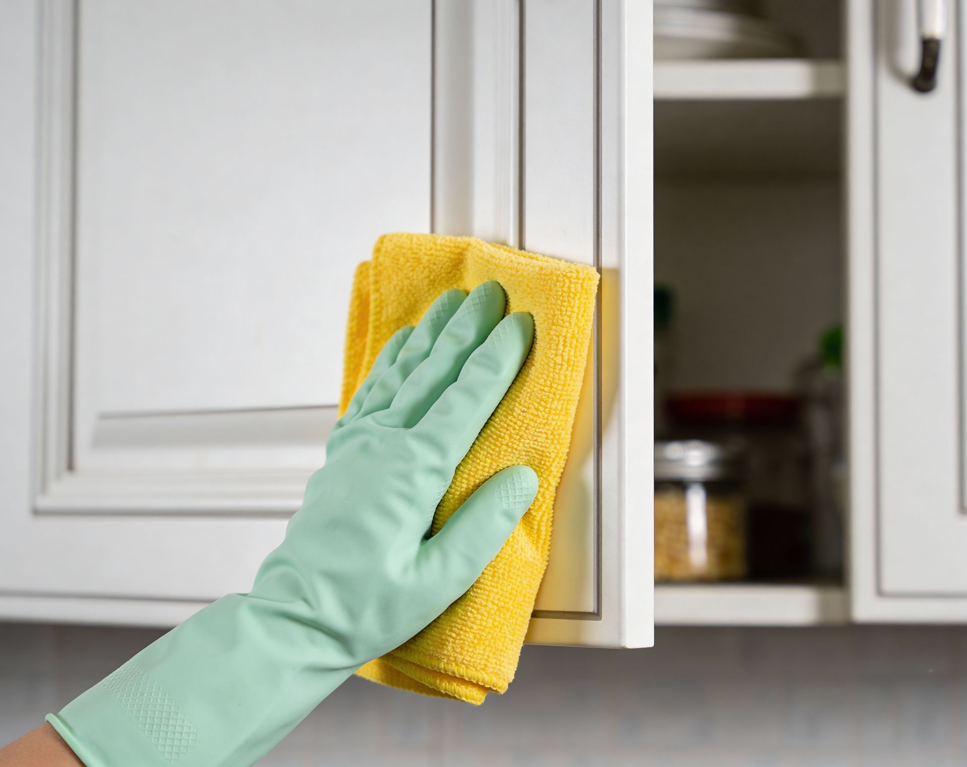 Gloved hand wiping a white kitchen cabinet with a yellow cloth