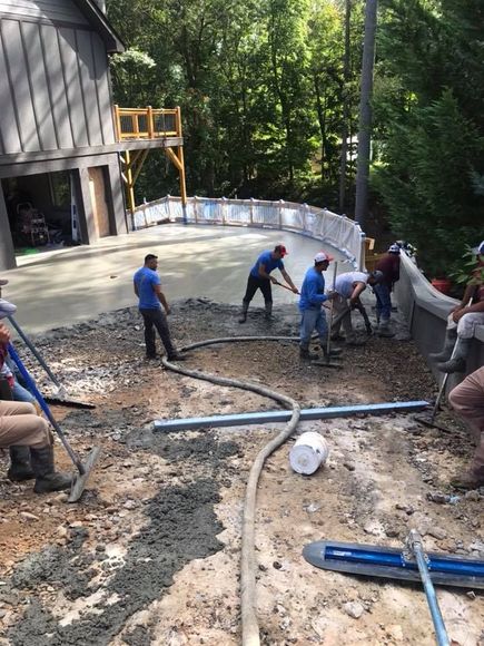 Construction workers pouring concrete on a curved surface outdoors; several use tools to smooth the cement.