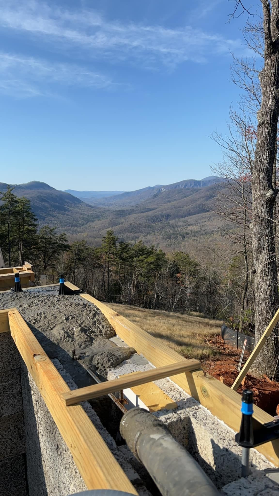 Construction site with concrete work on a hillside, overlooking a mountain range under a blue sky.
