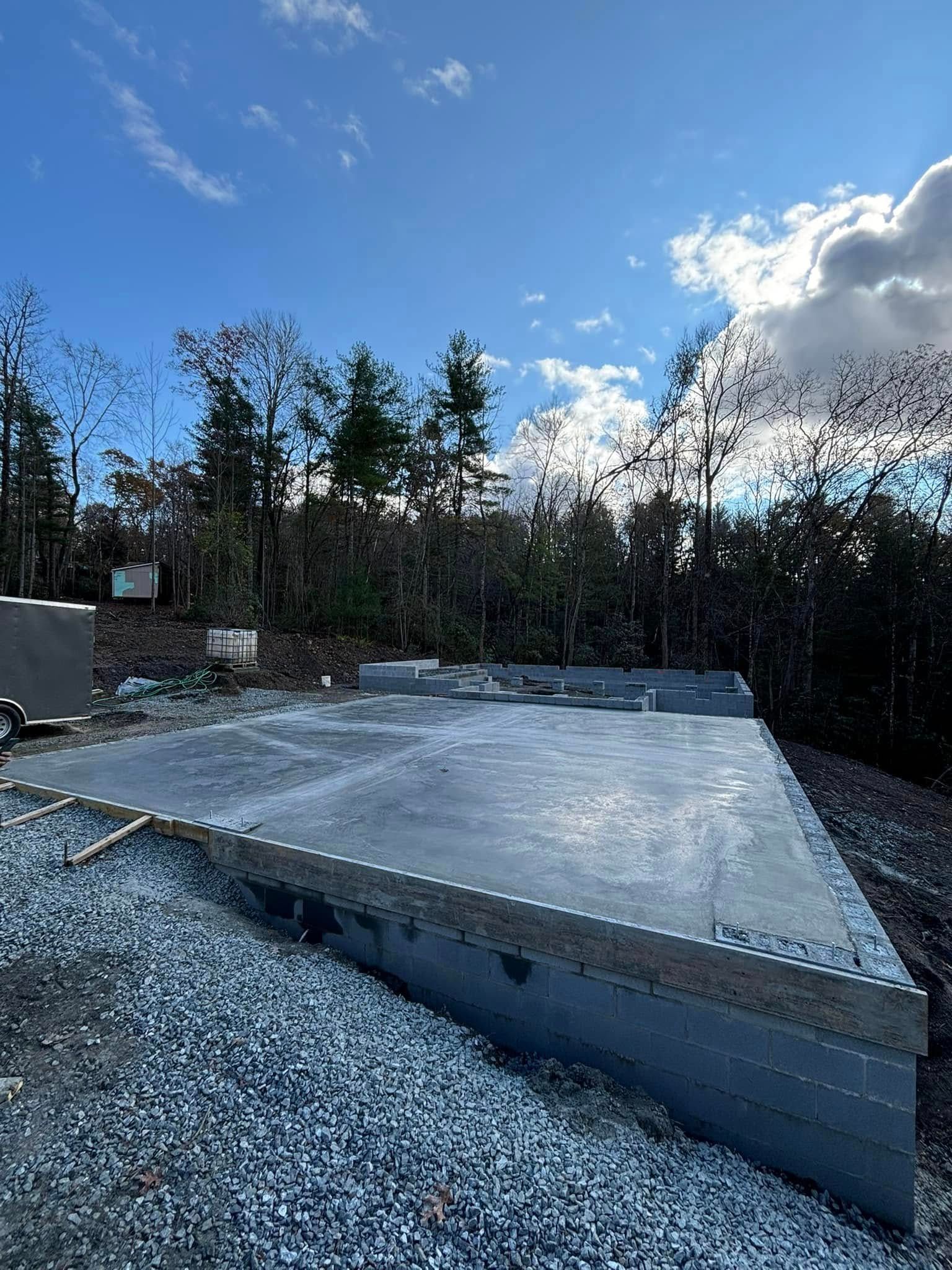 Concrete foundation with cinder block walls, construction site, trees and blue sky background.