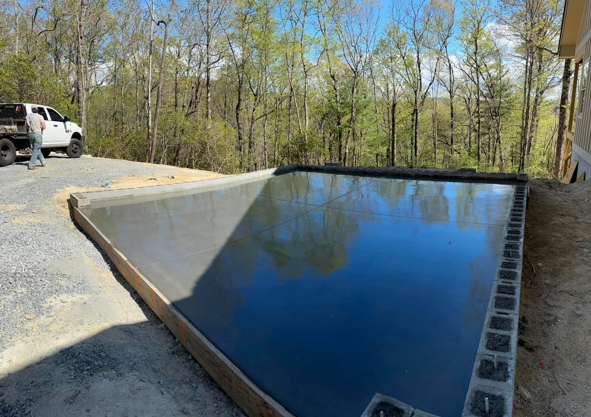 Freshly poured concrete surface; truck in the background, surrounded by gravel and trees.