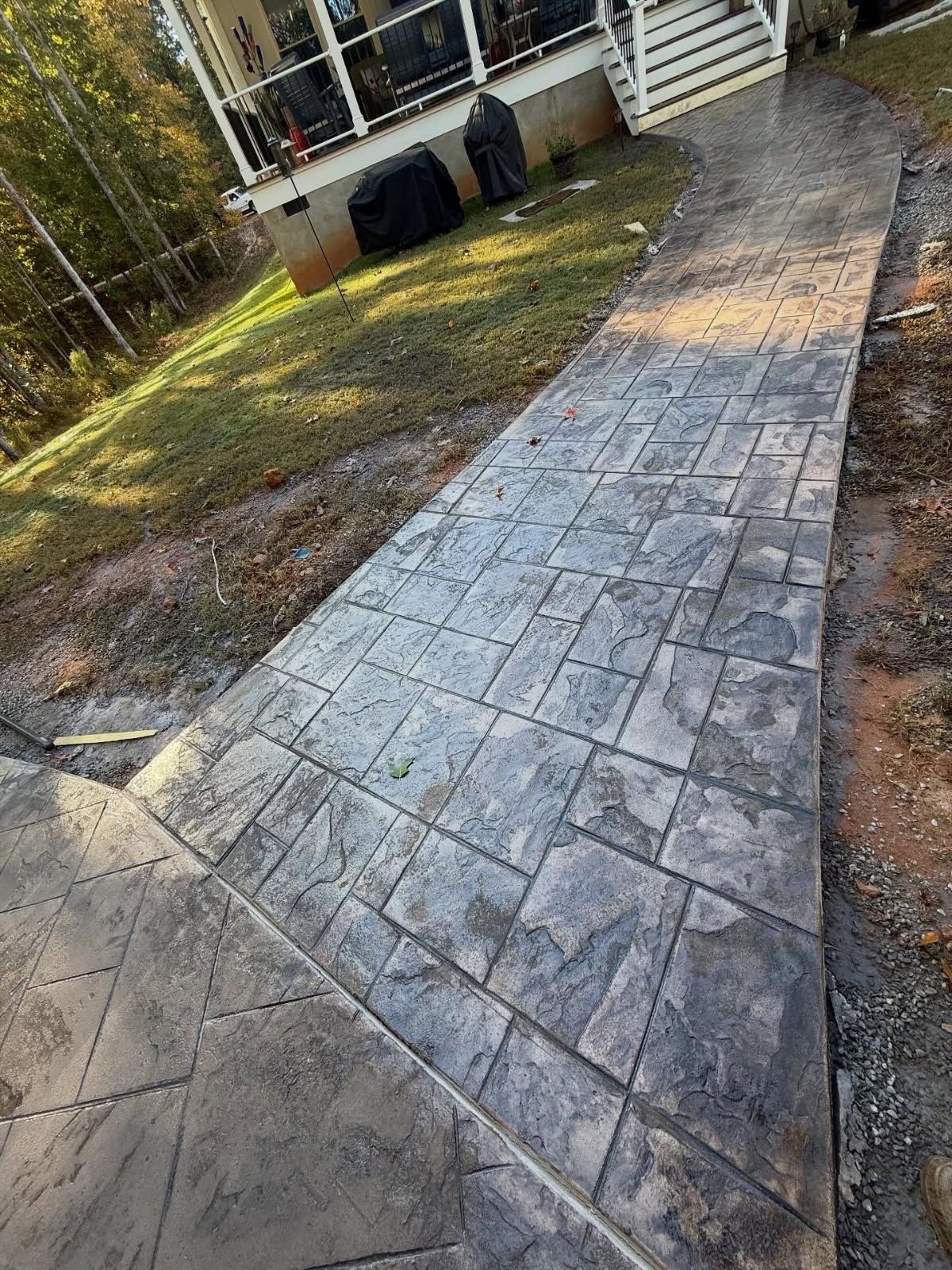 Stamped concrete walkway leading to a house, textured gray stone pattern.