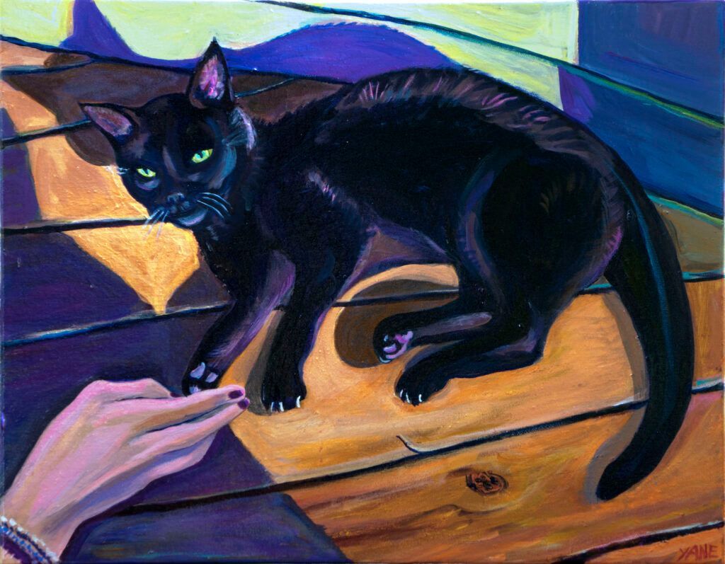 Black cat with green eyes and arched back, interacting with a human hand reaching out on a wood surface.