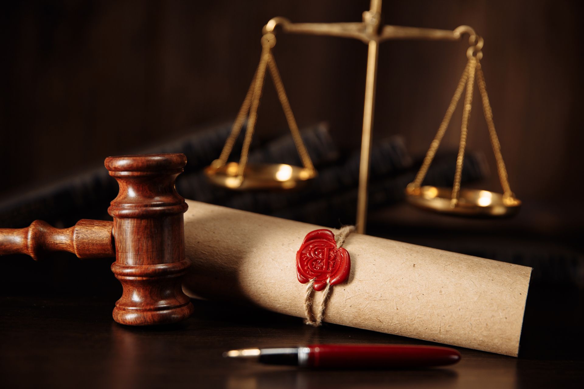 Gavel, scroll with red wax seal, balance scales, and pen on a dark surface.