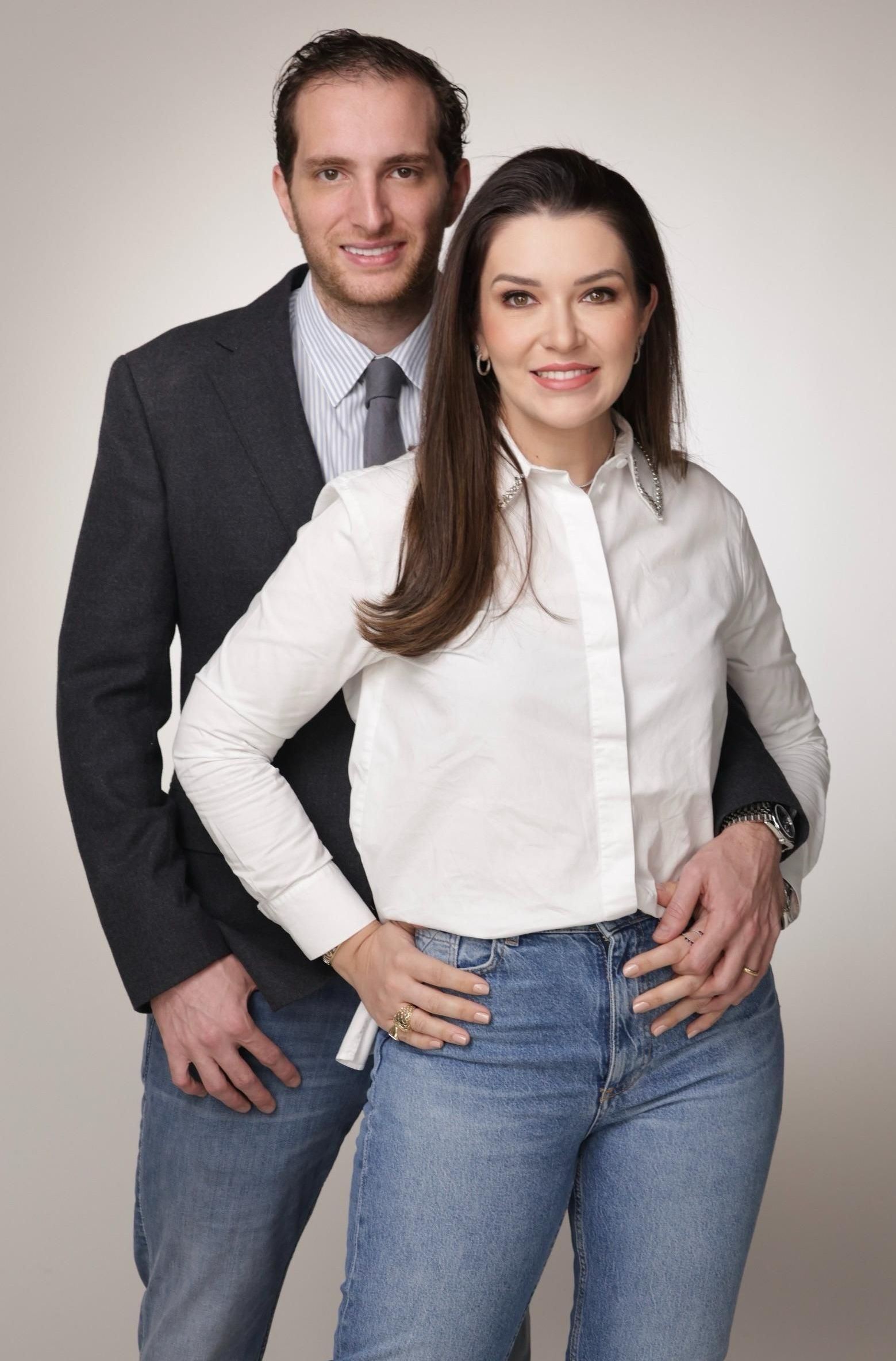 Um homem de terno e gravata está de pé ao lado de uma mulher de camisa branca e jeans.
