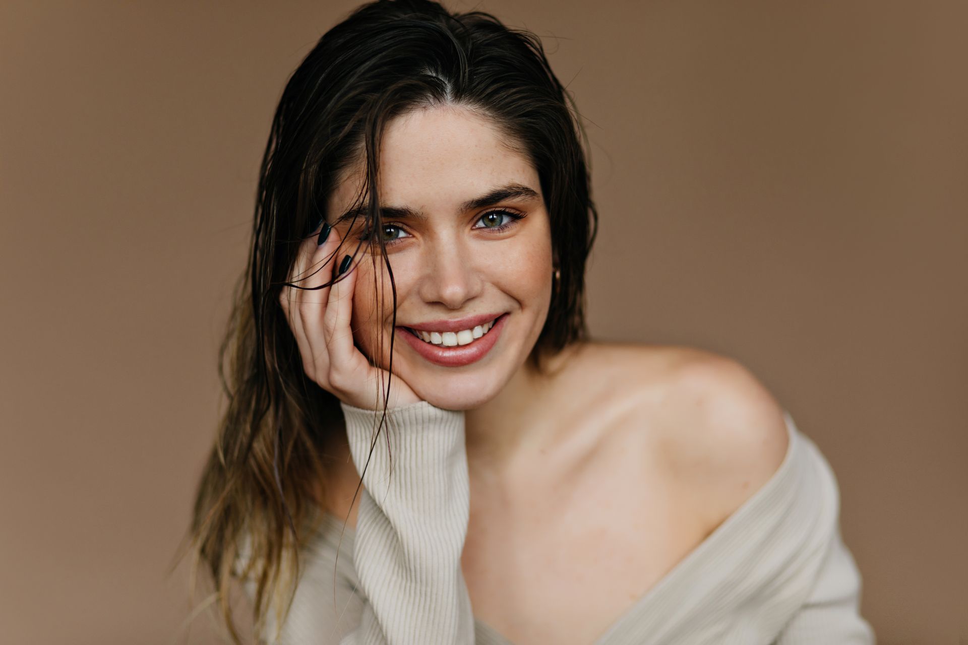 Uma mulher com um suéter branco está sorrindo com a mão no rosto.