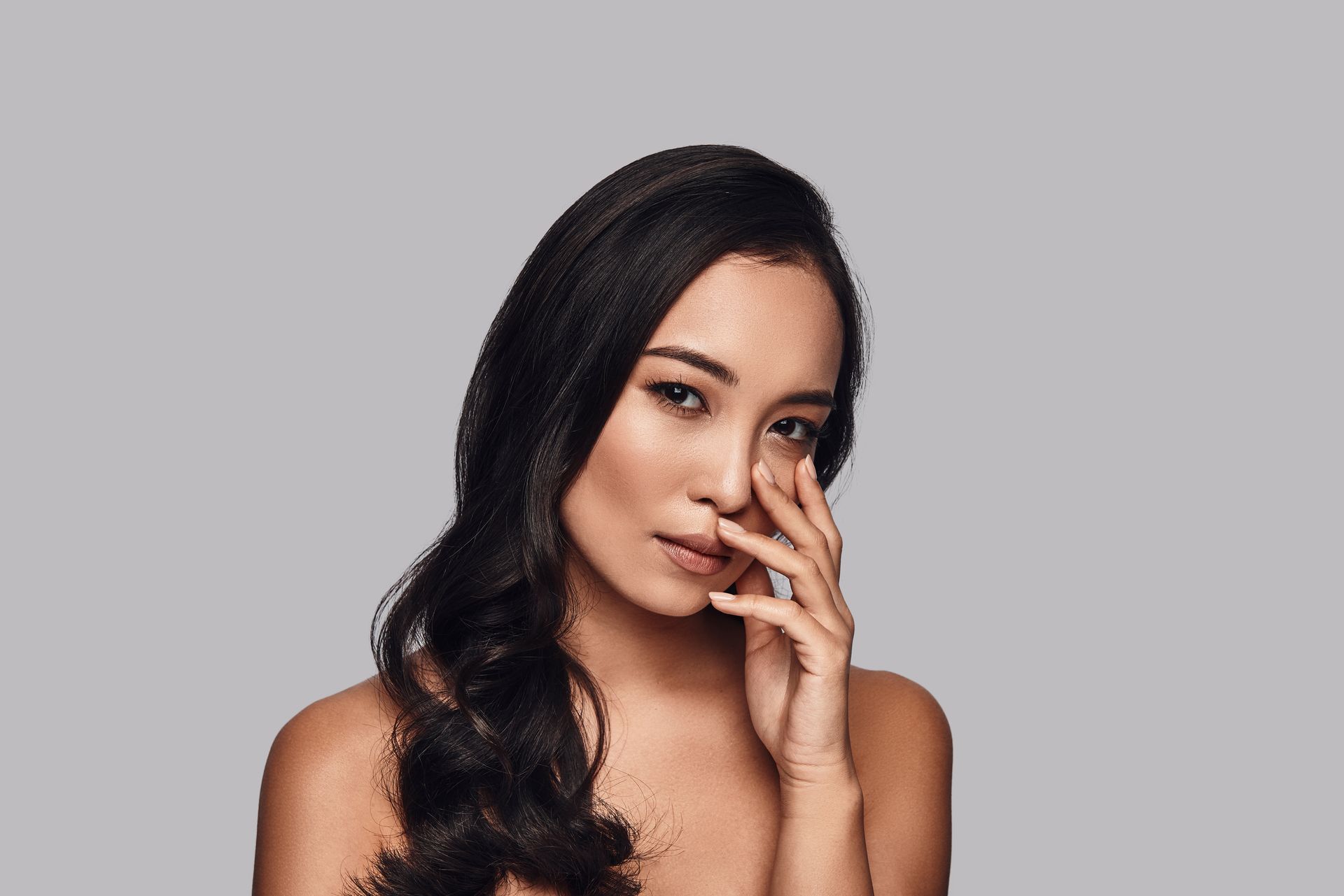 Uma mulher com longos cabelos pretos está cobrindo o rosto com a mão.