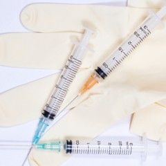 Three syringes with needles on top of a pair of beige medical gloves.