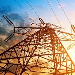 Power lines and a tall electricity pylon against a colorful sunset sky.