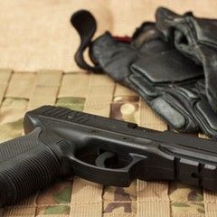 Black handgun and gloves on a camouflage surface.