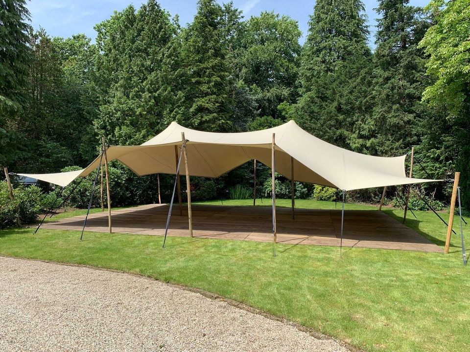 Zandkleurige stretchtent in een tuin bij een landhuis