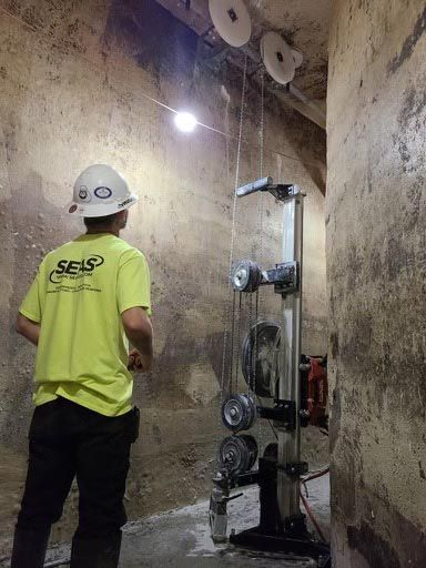 Worker in neon yellow shirt and hard hat inspecting machinery in a concrete industrial shaft.