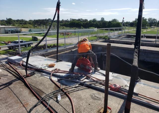 Construction worker in orange vest working on a rooftop beside cables and tools.