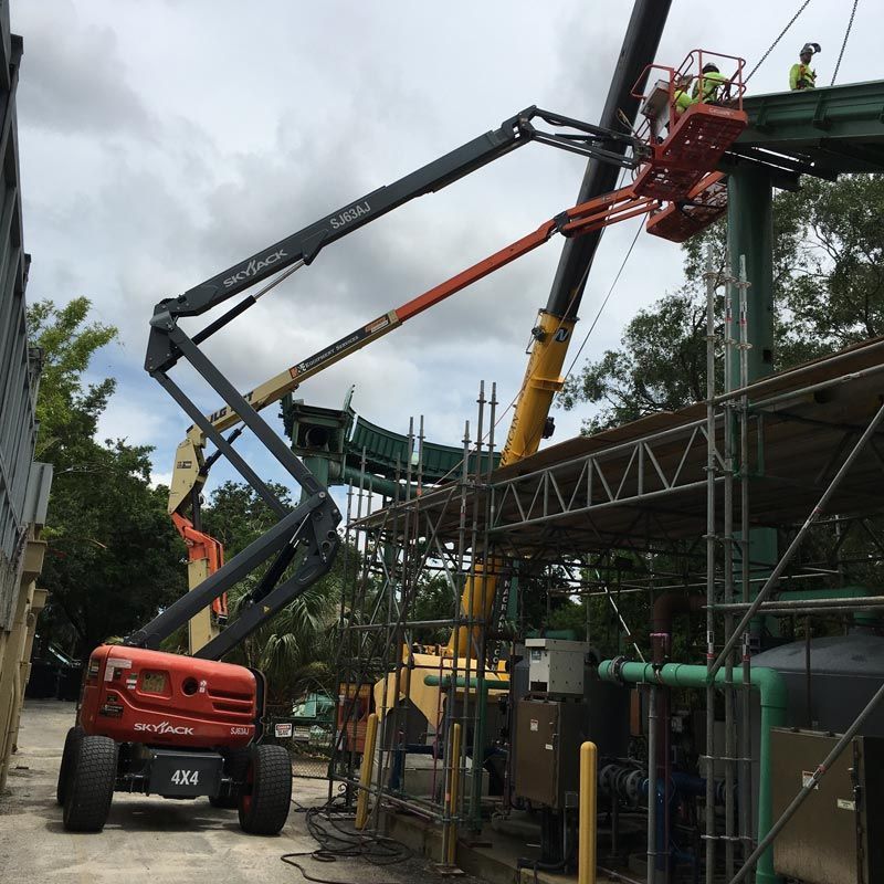 Red boom lift and workers on scaffolding beside a building under construction, with green canopy overhead