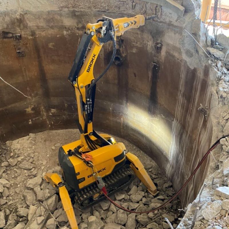 Yellow excavator working inside a deep circular excavation pit with rocky debris.