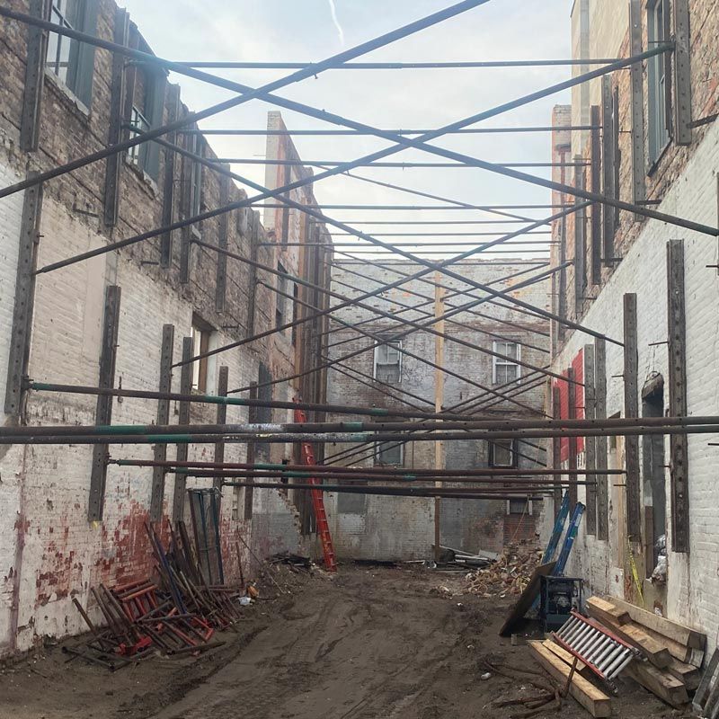Narrow construction alley between brick buildings with metal scaffolding and scattered materials