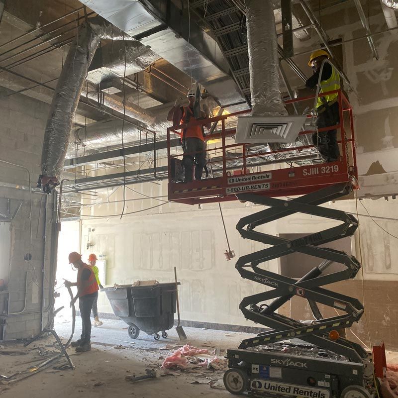 Construction workers on scissor lifts installing ductwork in a partially renovated room
