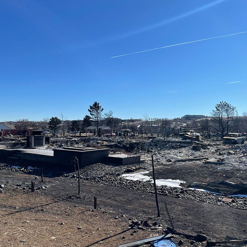 Burned landscape with charred debris and collapsed structures under a clear blue sky