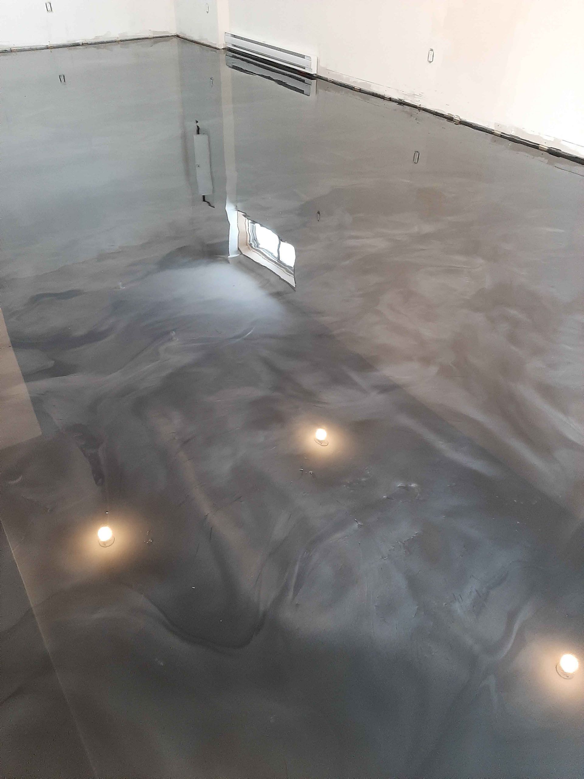 A shiny metallic floor in a room with a reflection of a window.