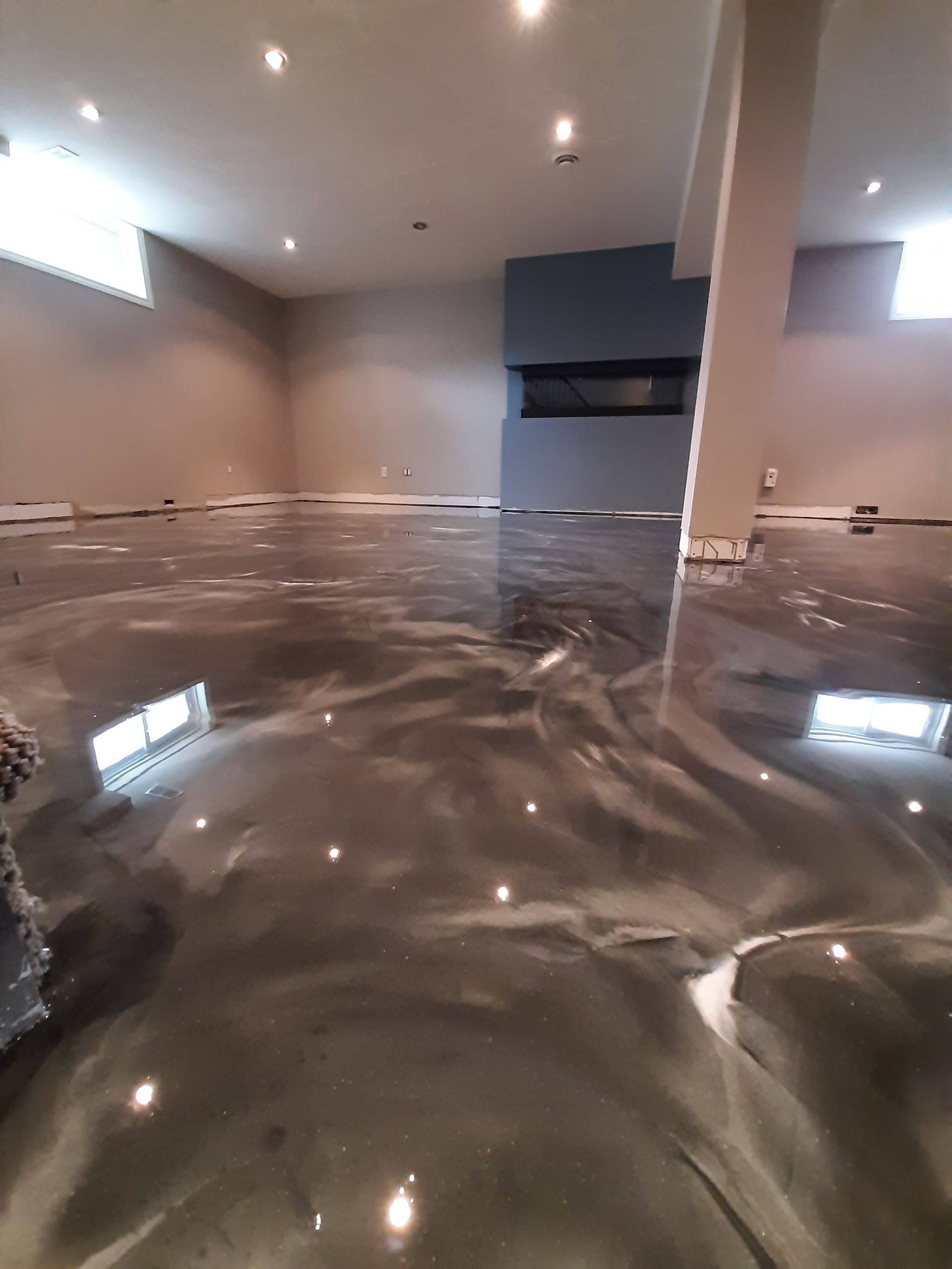 A basement with a shiny metallic floor and a fireplace.