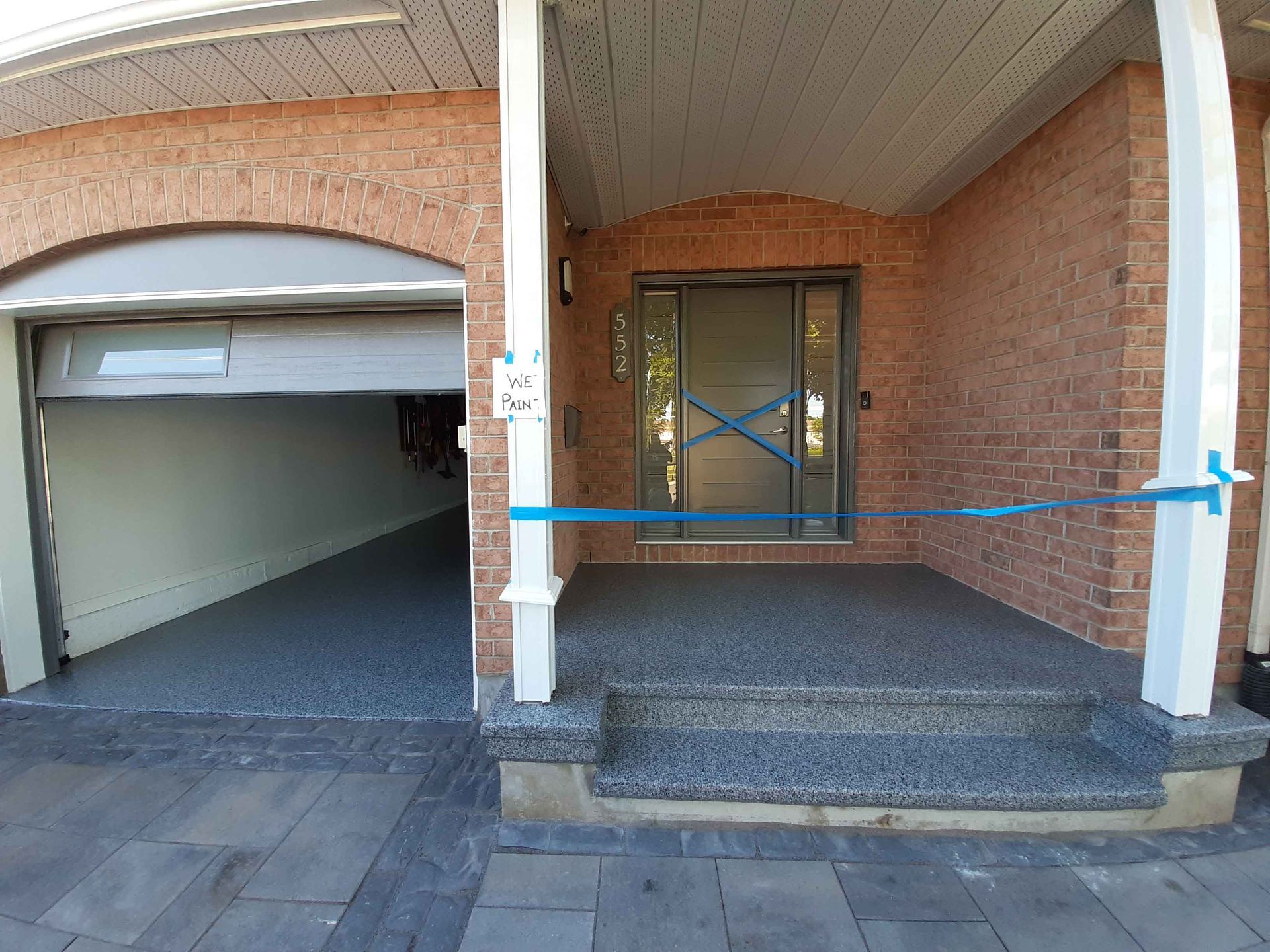 A brick house with a garage and a porch with blue tape on it.
