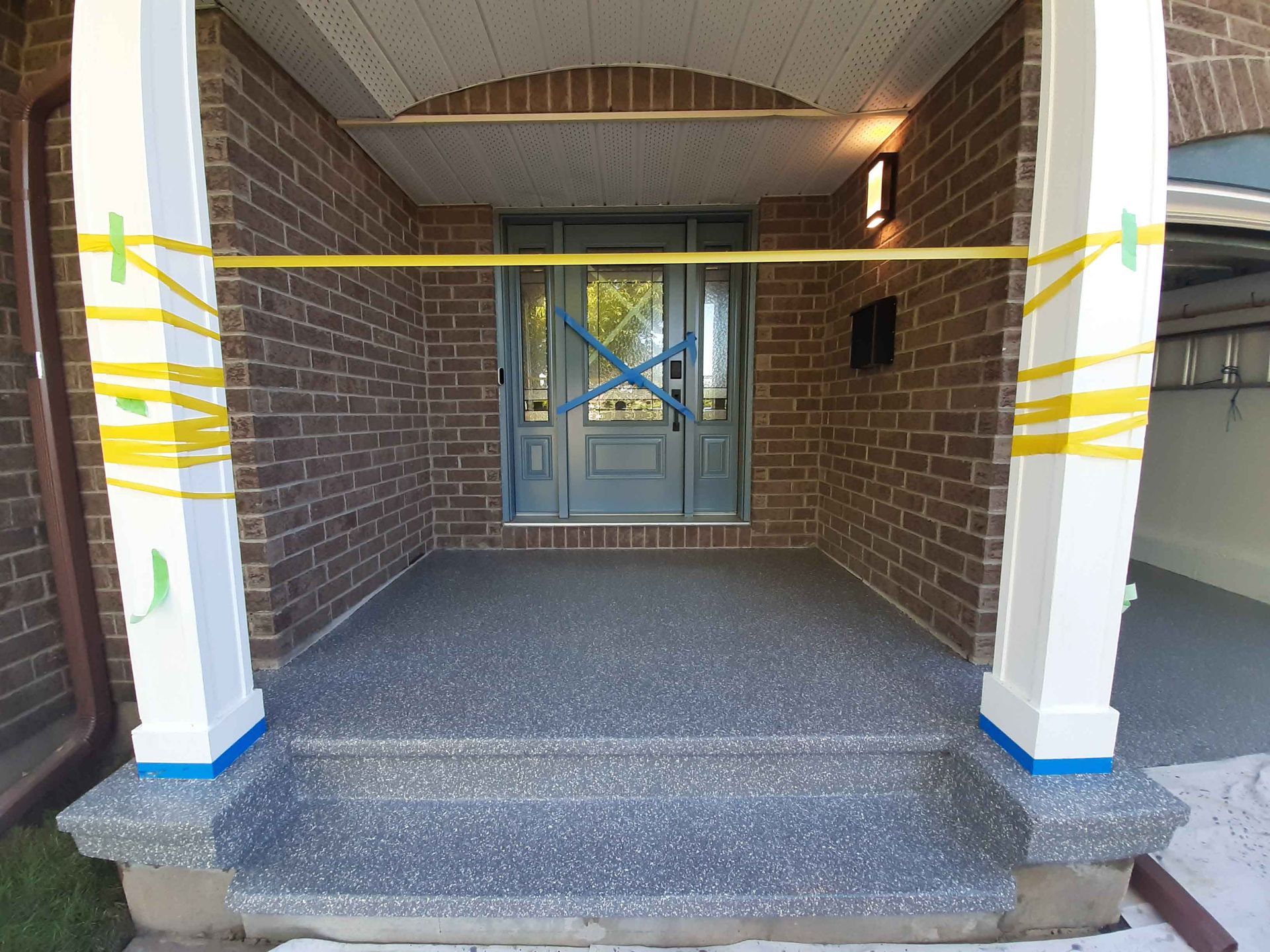 A front porch of a brick house with a blue door and steps covered in tape.