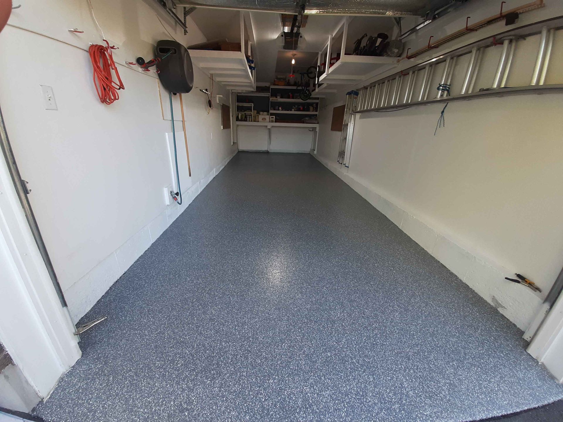 A garage with a ladder hanging from the ceiling and a gray floor.