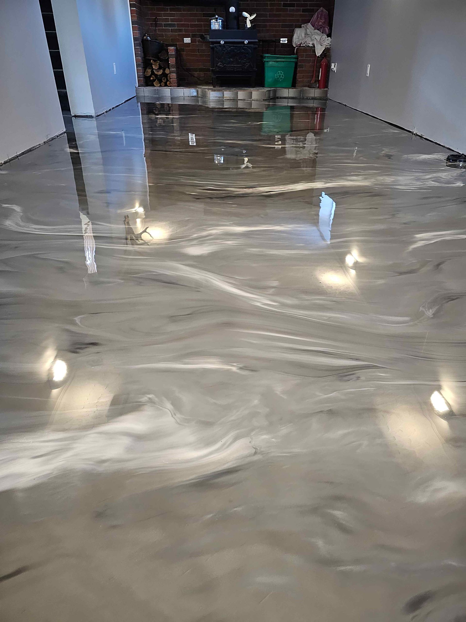 A shiny metallic floor in a basement with a fireplace in the background.