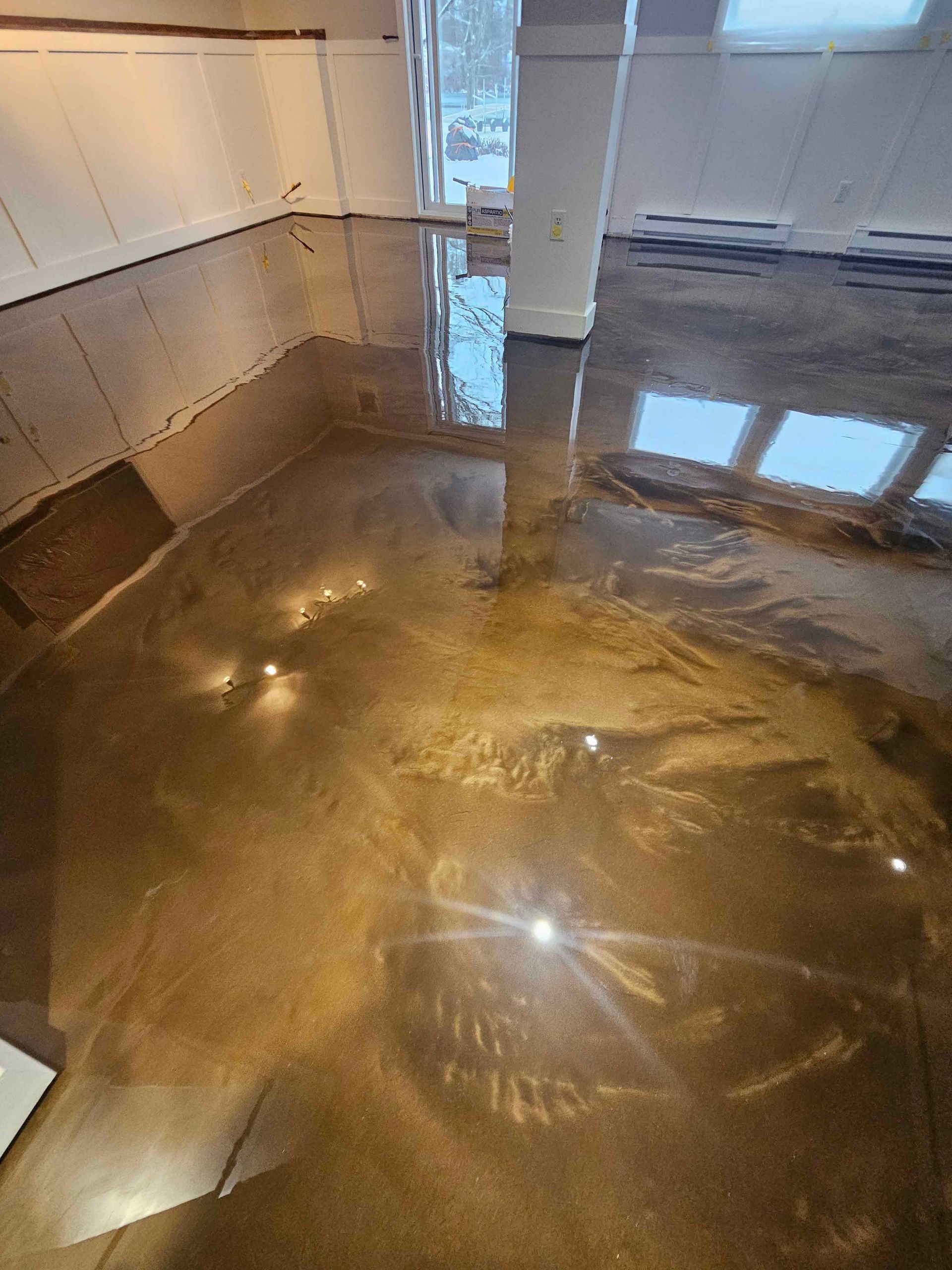 A room with a shiny metallic floor and a reflection of a window.