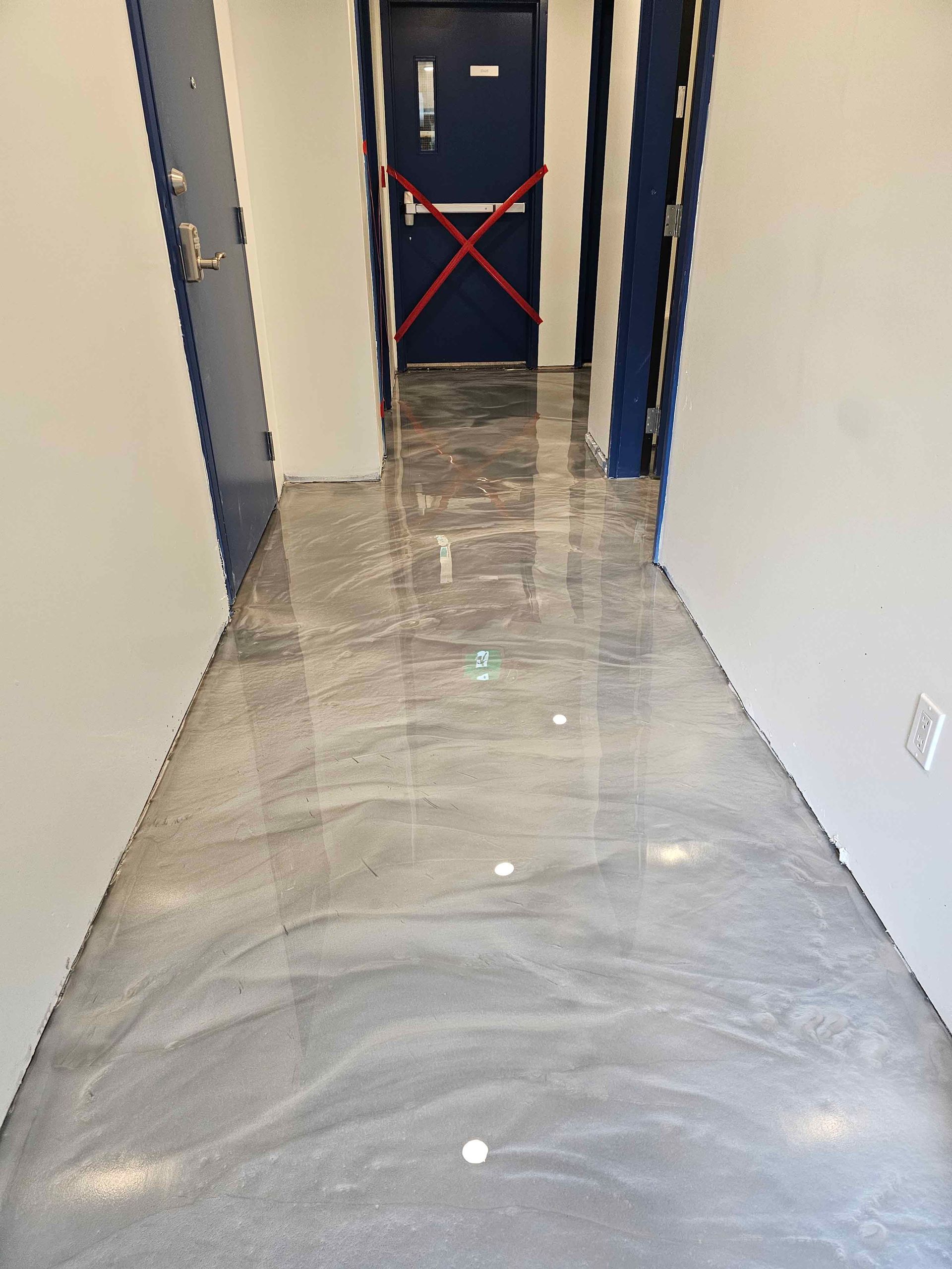 A hallway with a shiny metallic floor and a blue door.