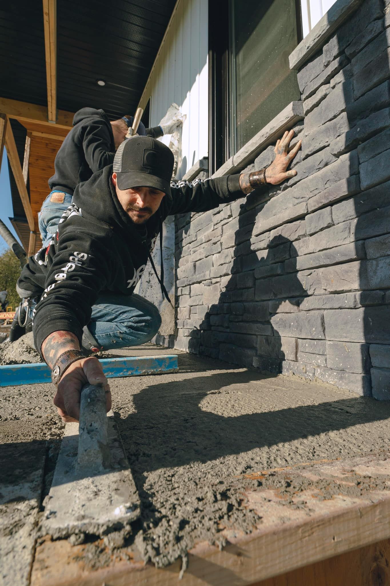 A man is kneeling down next to a brick wall.