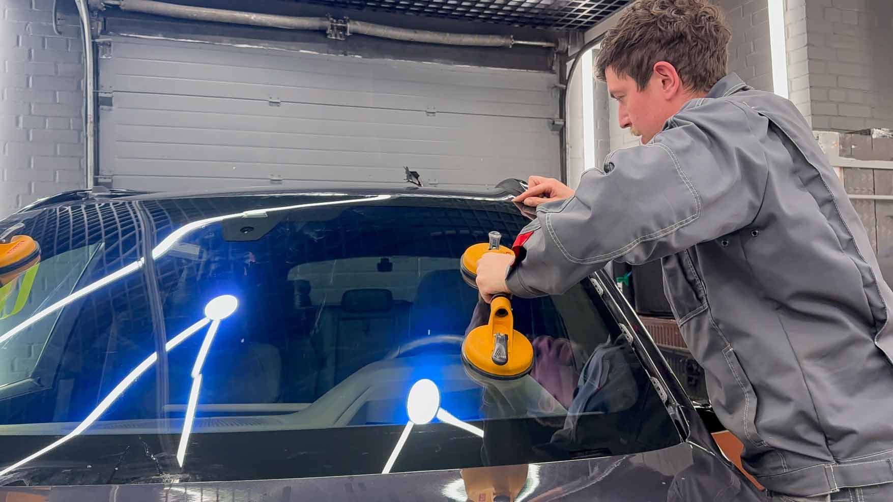 Technician replacing the windshield of a car in an auto service station garage with suction cups. Technician replacing the windshield of a car in an auto service station garage with suction cups.