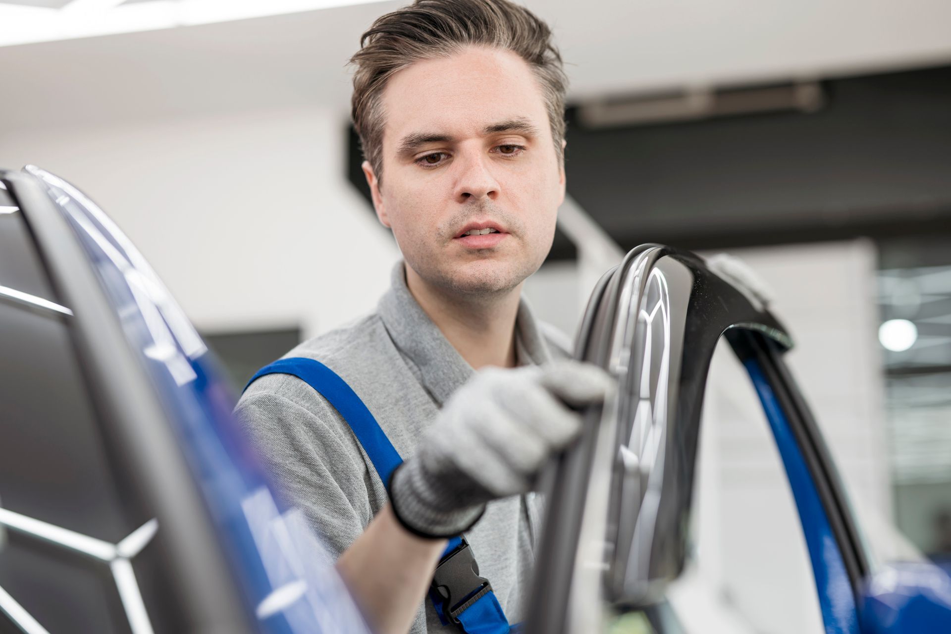 Technician performing car window replacement on a blue vehicle inside a garage workshop. Technician performing car window replacement on a blue vehicle inside a garage workshop.