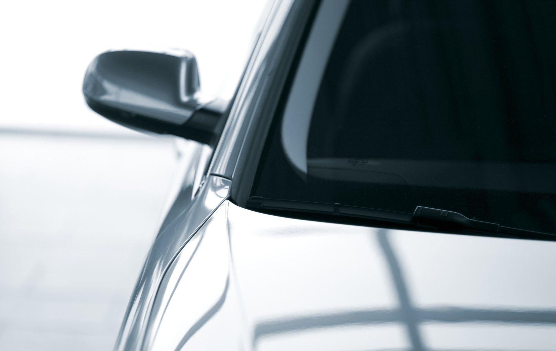 Close-up of the side of a silver car with a side mirror visible. The windshield and upper body are also in view.