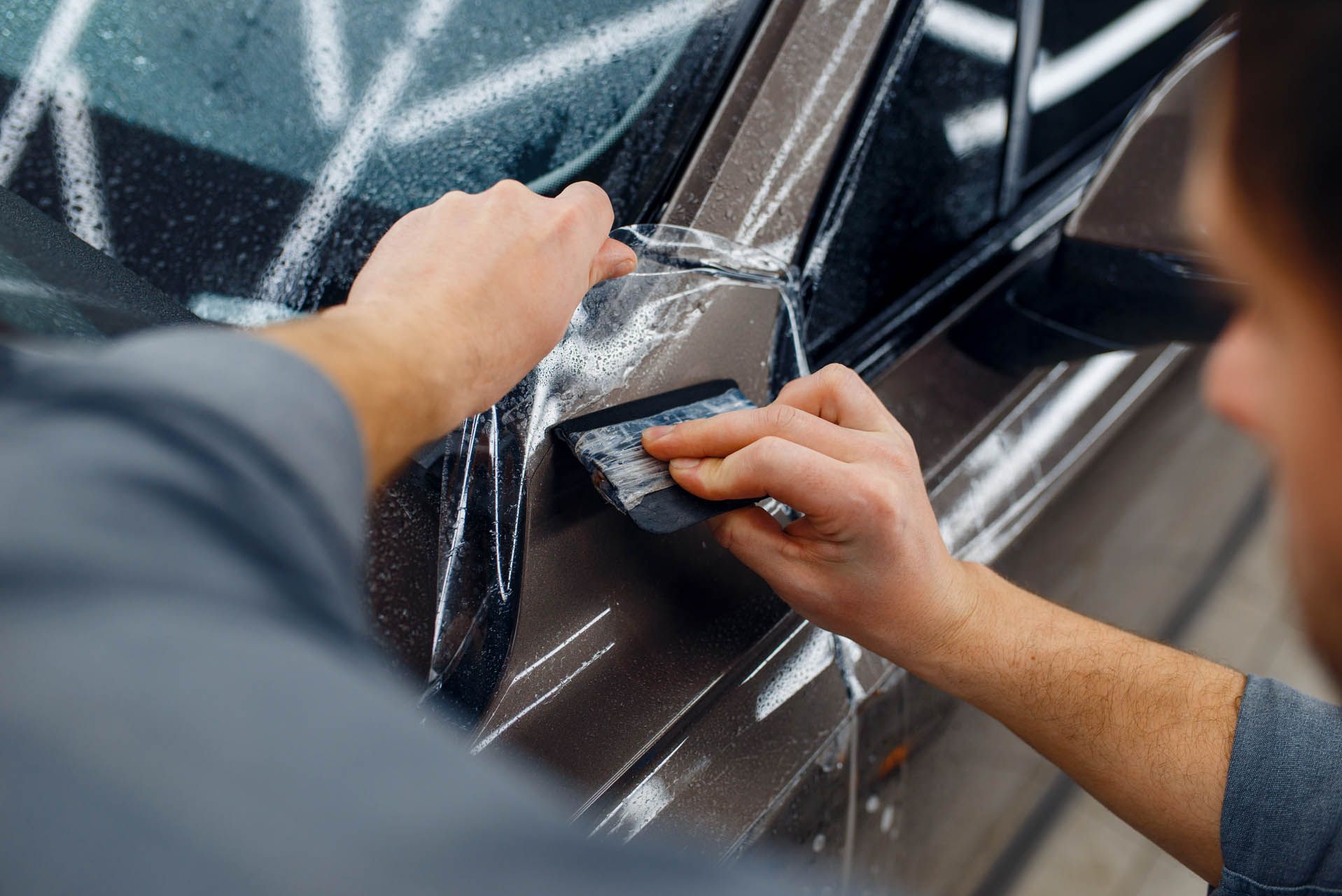 Hands applying protective film to a dark car door handle and side panel