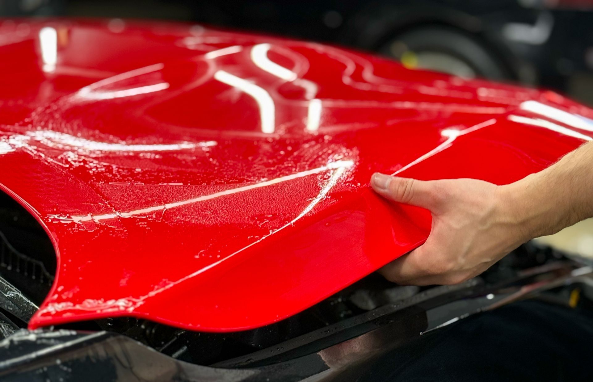 Hand polishing glossy red car body panel in an auto shop