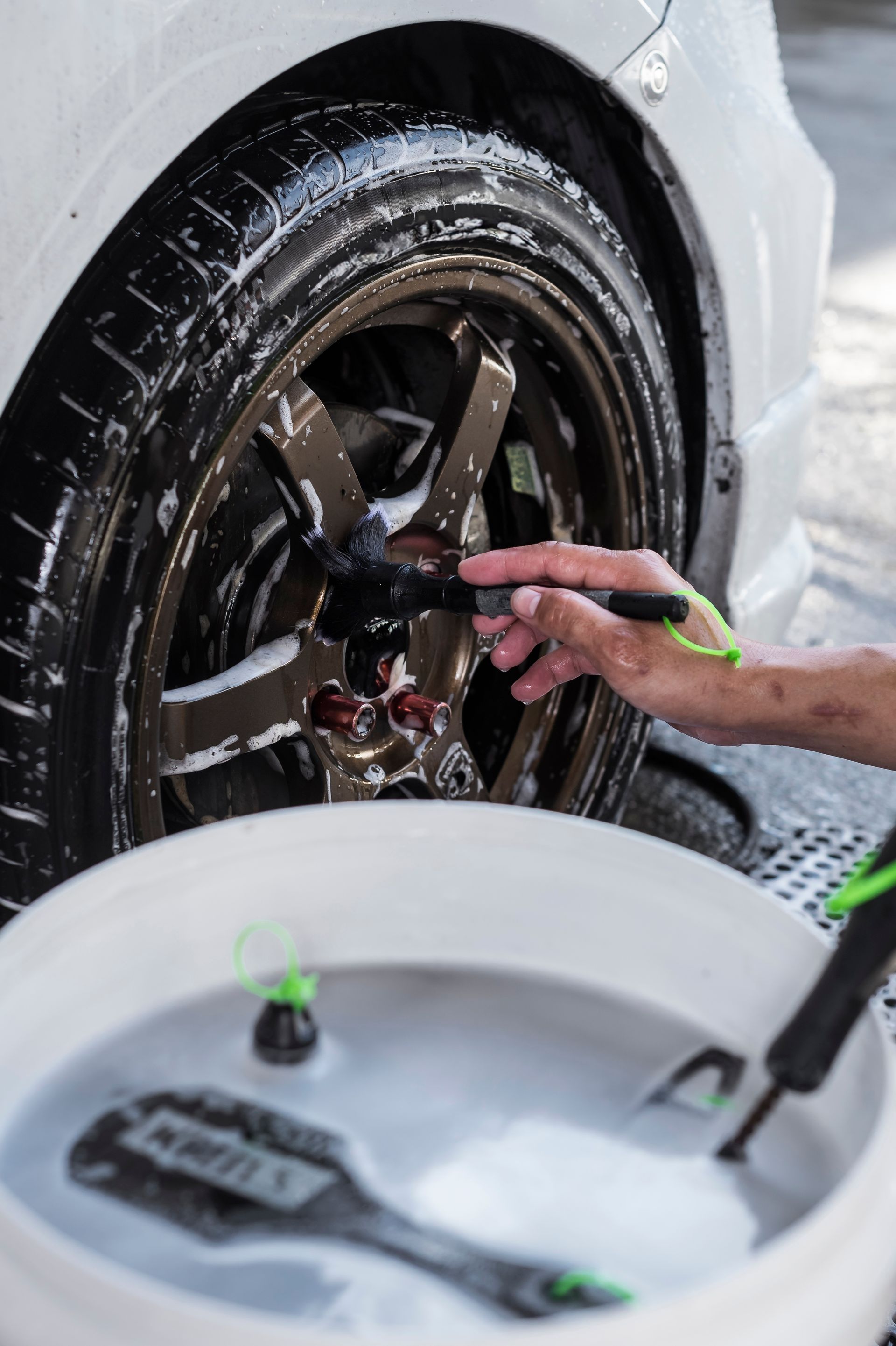 Person cleaning a black car wheel with soap and water outdoors