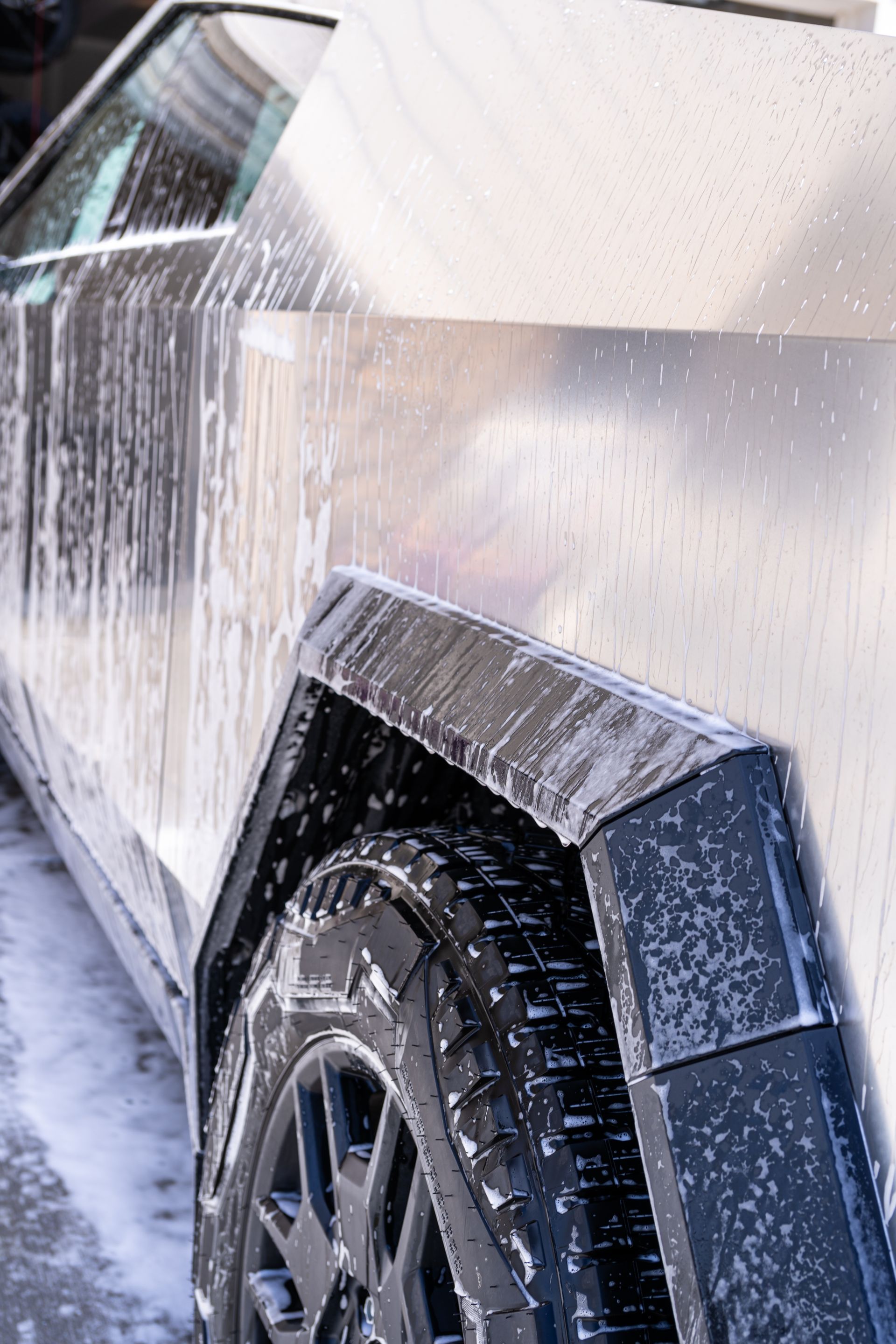 White SUV being washed with water spray, close-up of rear wheel and side panel
