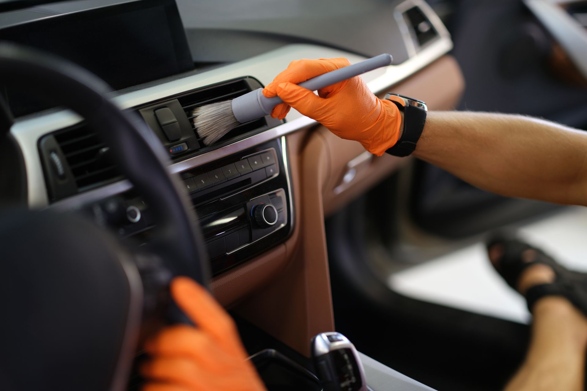 Gloved hands cleaning a car dashboard with a spray bottle and cloth
