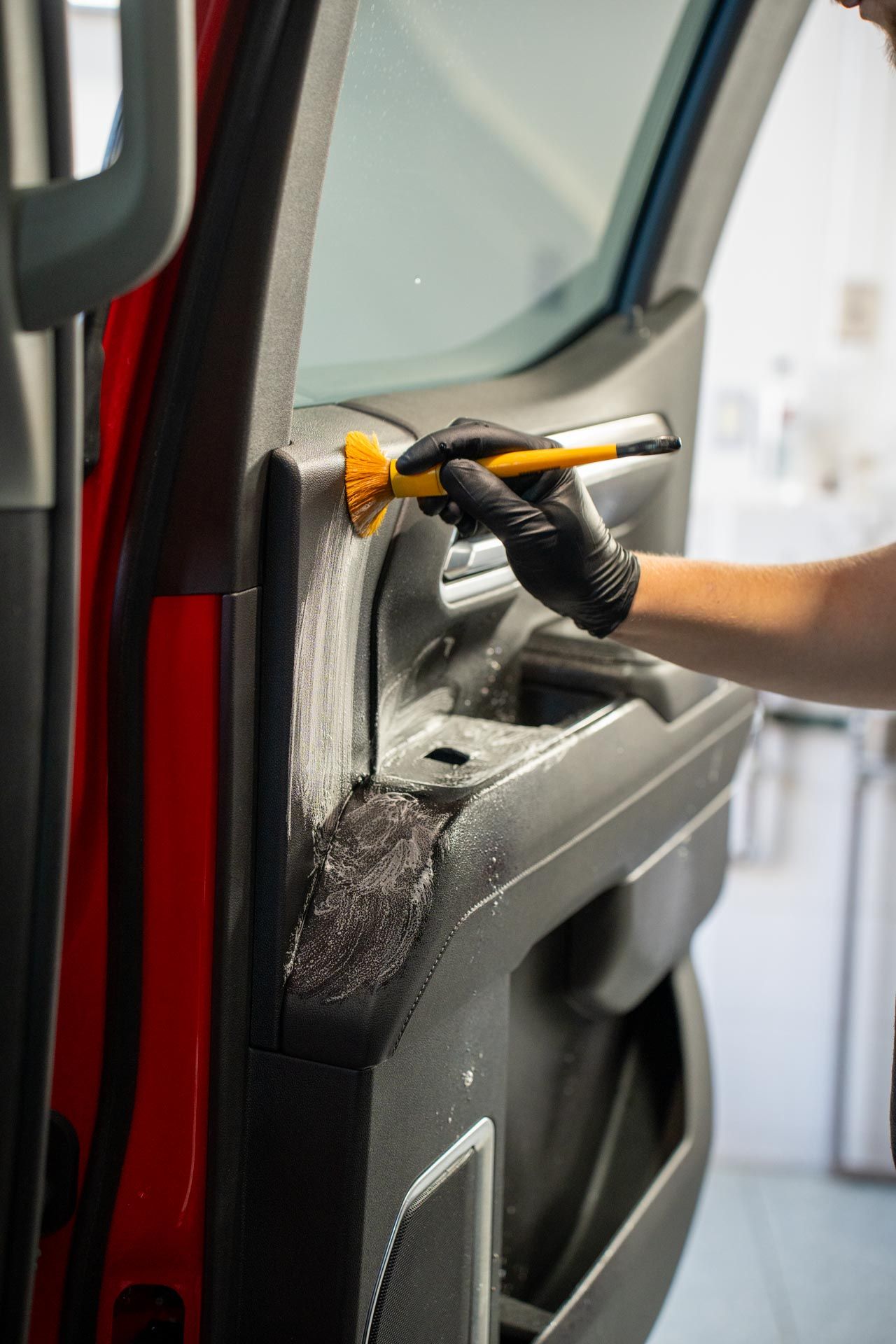 Gloved hand cleaning a car door interior panel with a brush and spray in a workshop