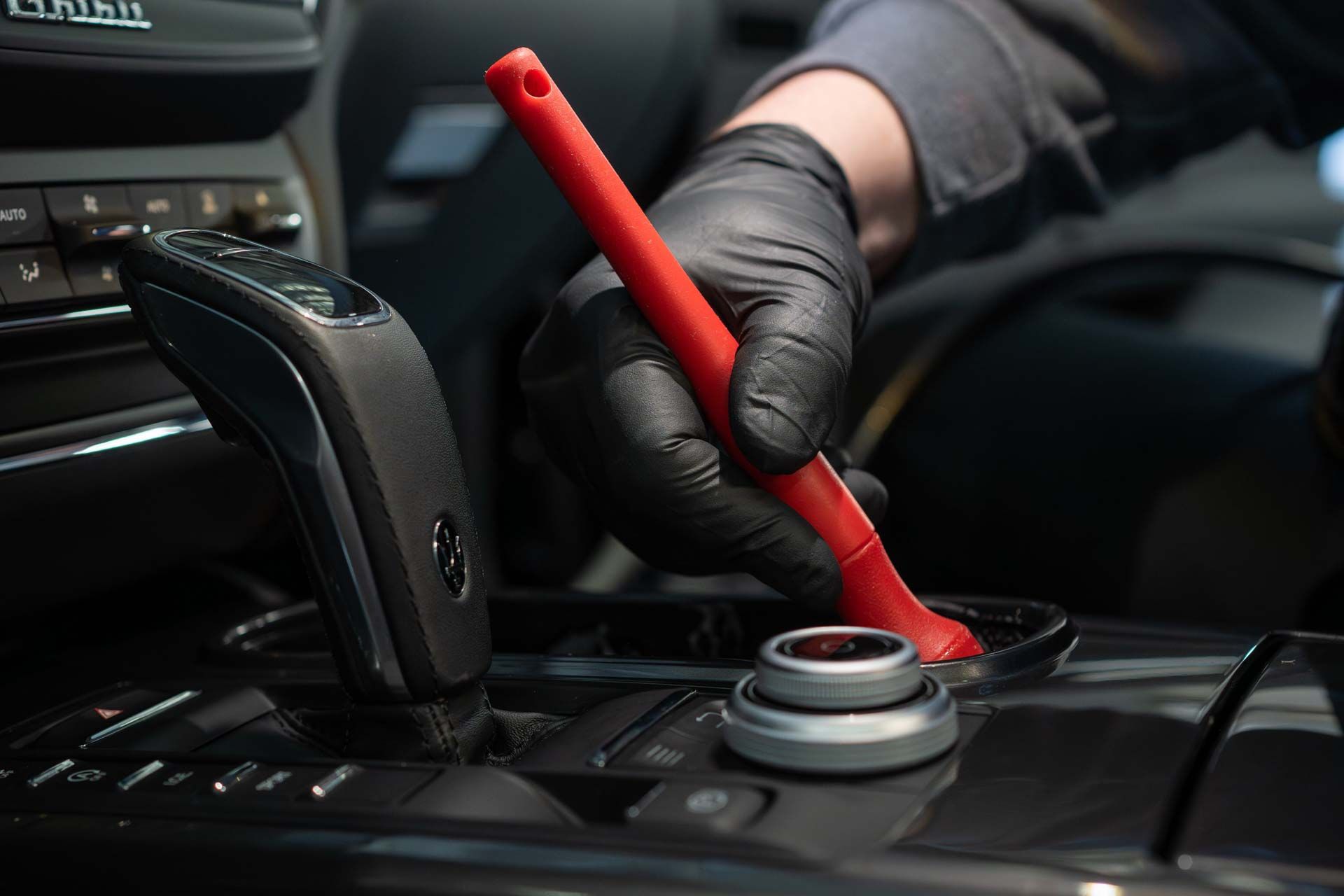Gloved hand using a red tool on a car’s center console near the gear shift