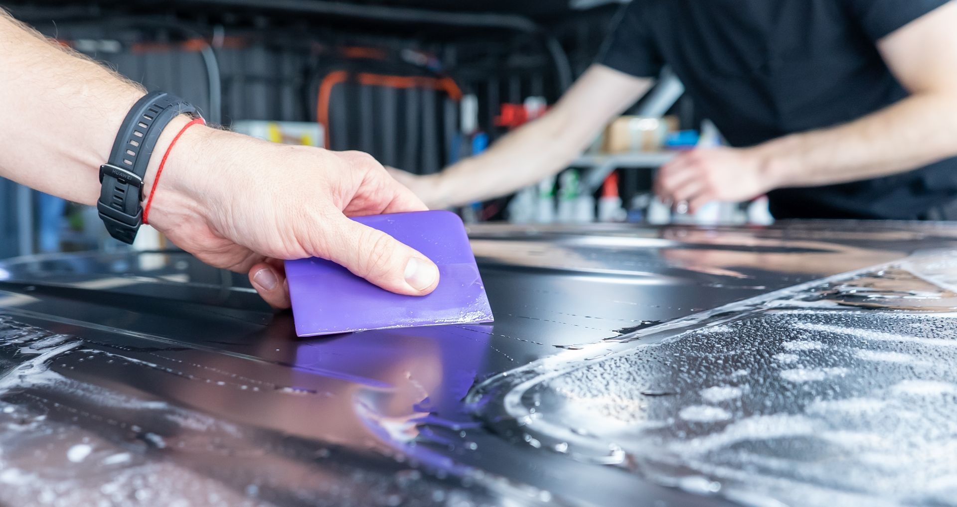 Hand wiping a glossy black car surface with a purple sponge in a garage