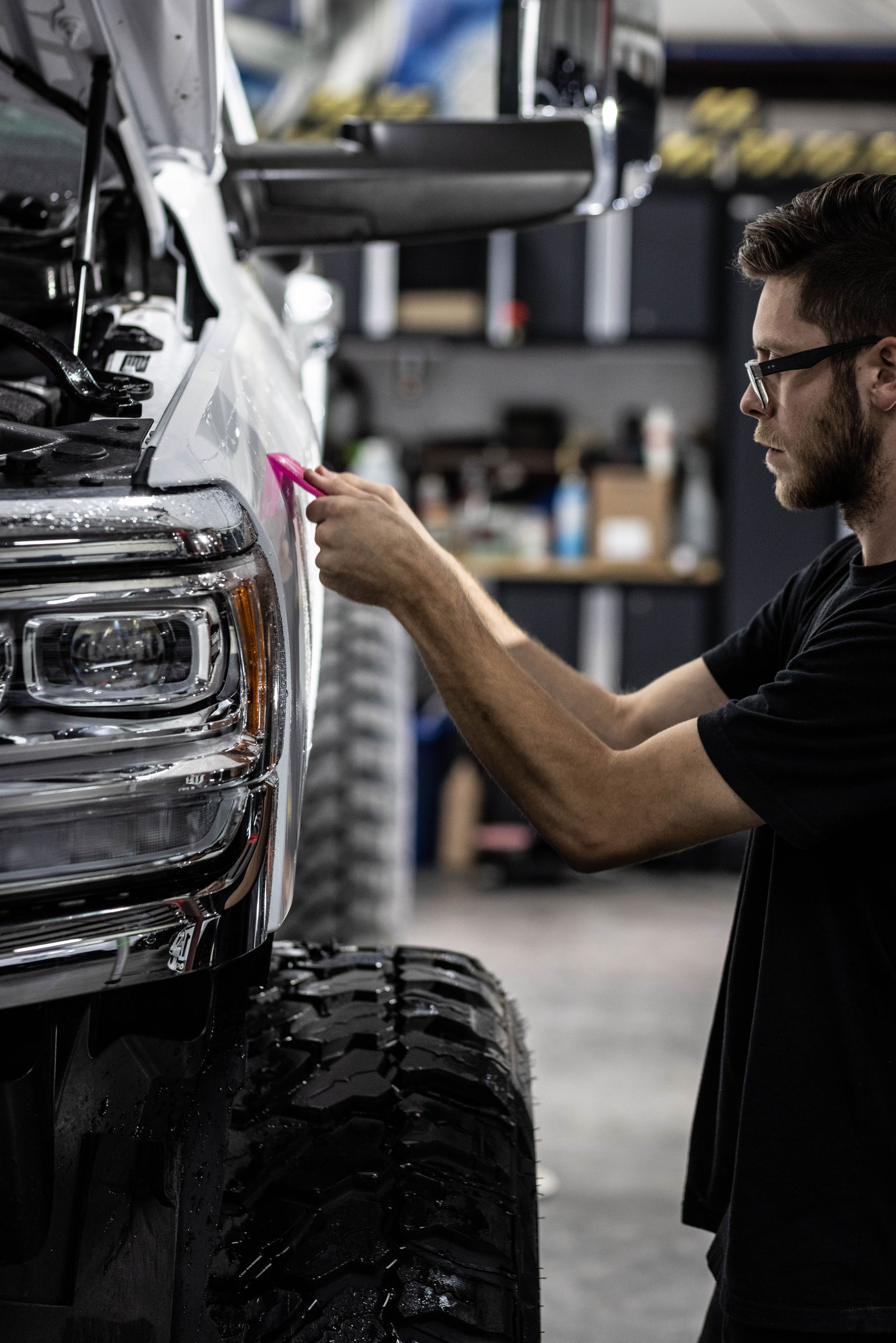 Mechanic polishing a white truck’s front end in a garage, using a pink cloth