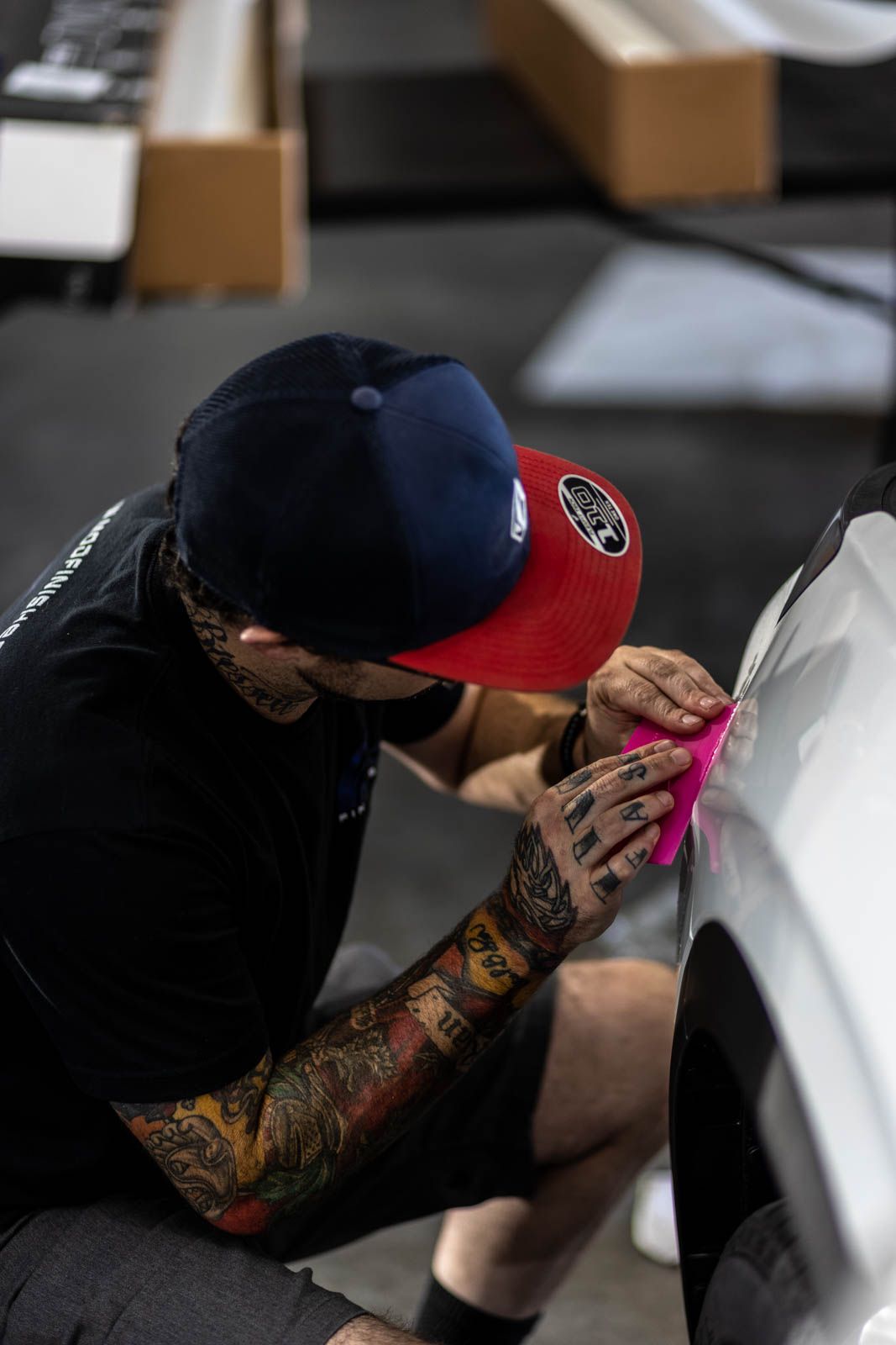 Person kneeling and applying bright pink tape to a white car in a workshop