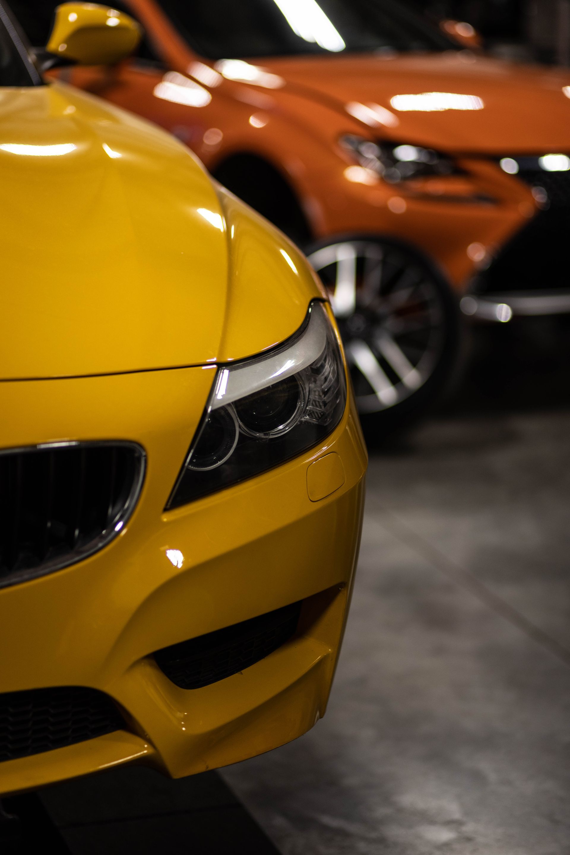 Yellow sports car in foreground with orange sports car blurred behind in a showroom