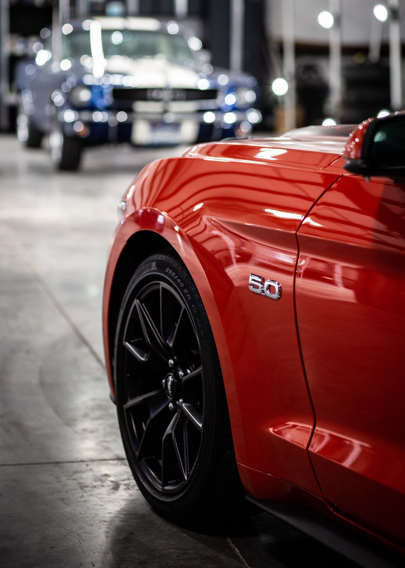 Red sports car with black wheel in a showroom, with a blue car blurred in the background