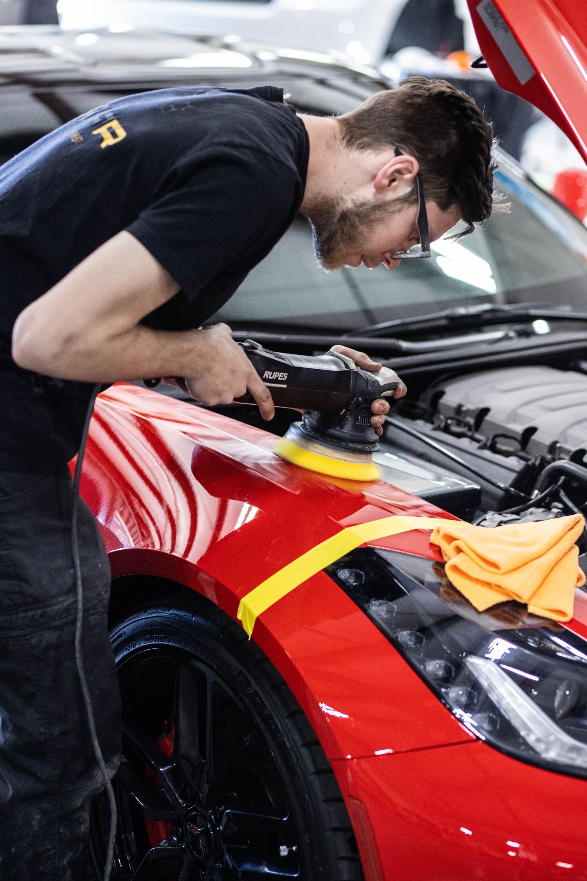 Mechanic inspecting red sports car engine under open hood in a workshop