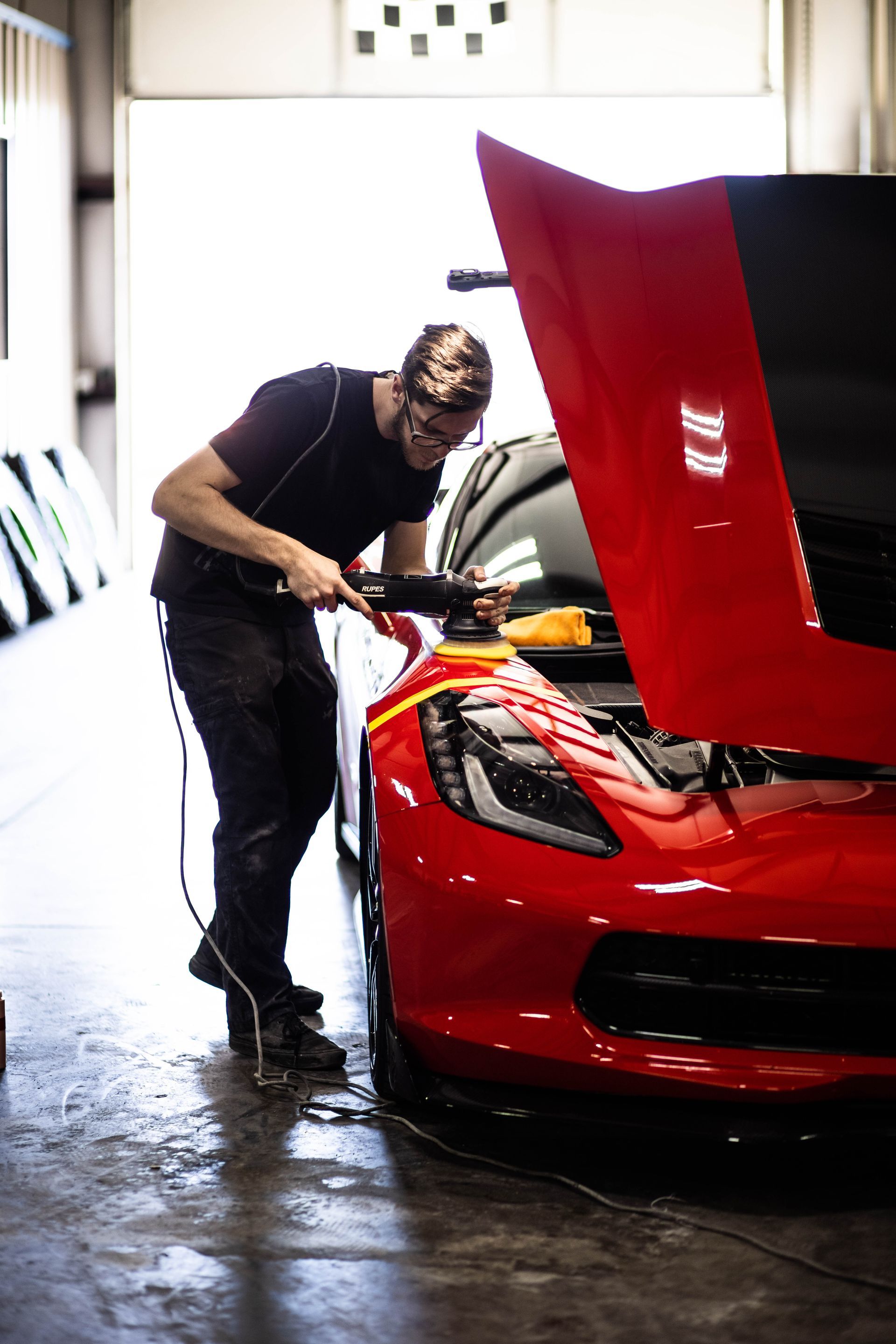 Mechanic cleaning a red sports car with its hood open in a garage