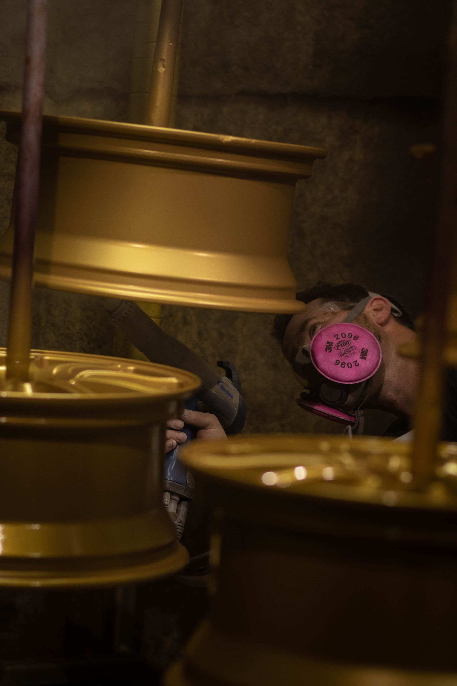 Pink worker ear protection among stacked gold metal drums in a dim industrial setting